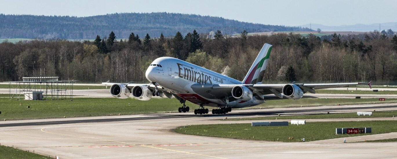 Emirates Airbus A380 taking off in daylight at Zurich Airport with scenic backdrop.